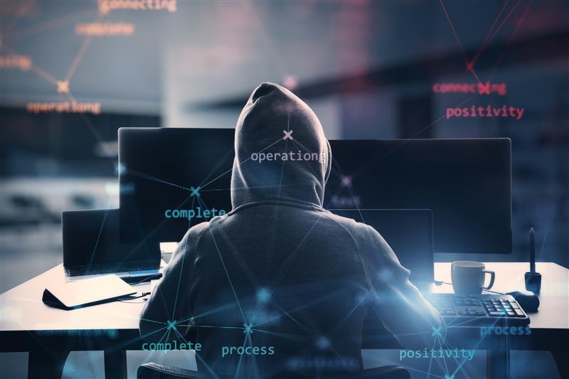 A person in a hoodie sits at a desk with multiple screens, surrounded by text like "operation" and "positivity." Dark, computer-focused mood.