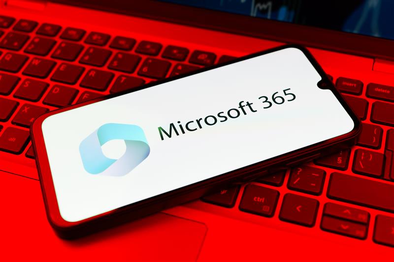 Smartphone displaying "Microsoft 365" logo on a glowing red laptop keyboard, creating a vibrant tech-focused scene.