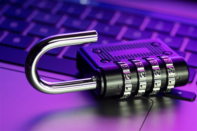 Open combination lock on a laptop keyboard, bathed in purple light. Numbers are visible on the lock dials, suggesting security themes.