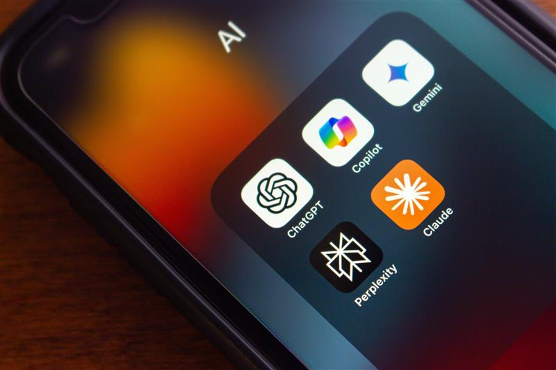 Smartphone screen showing AI app folder with icons for ChatGPT, Gemini, Copilot, and Claude against a blurred orange-red background.