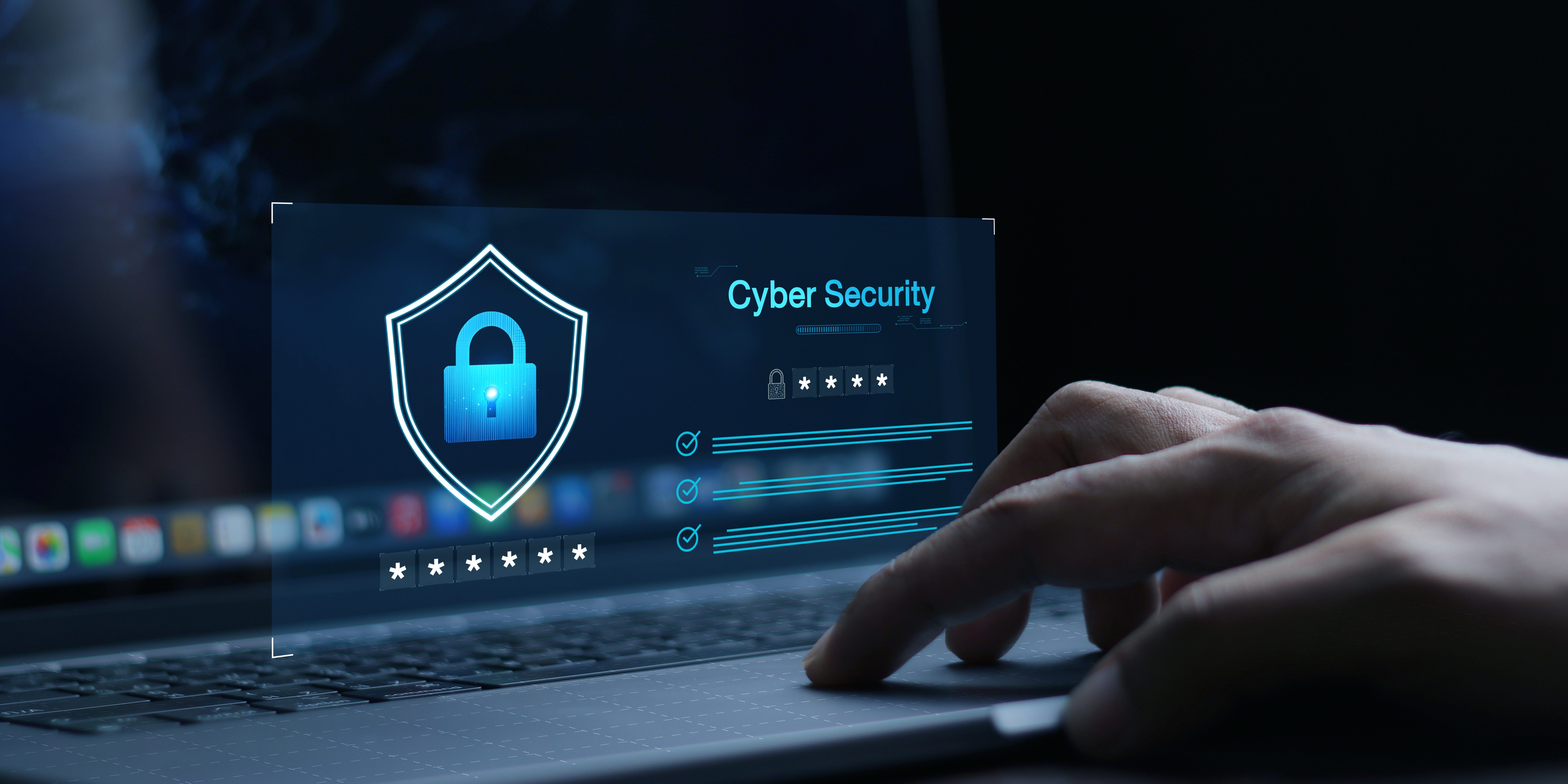 Hand types on laptop with a holographic display showing a shield and the text "Cyber Security." Dark background enhances focus.