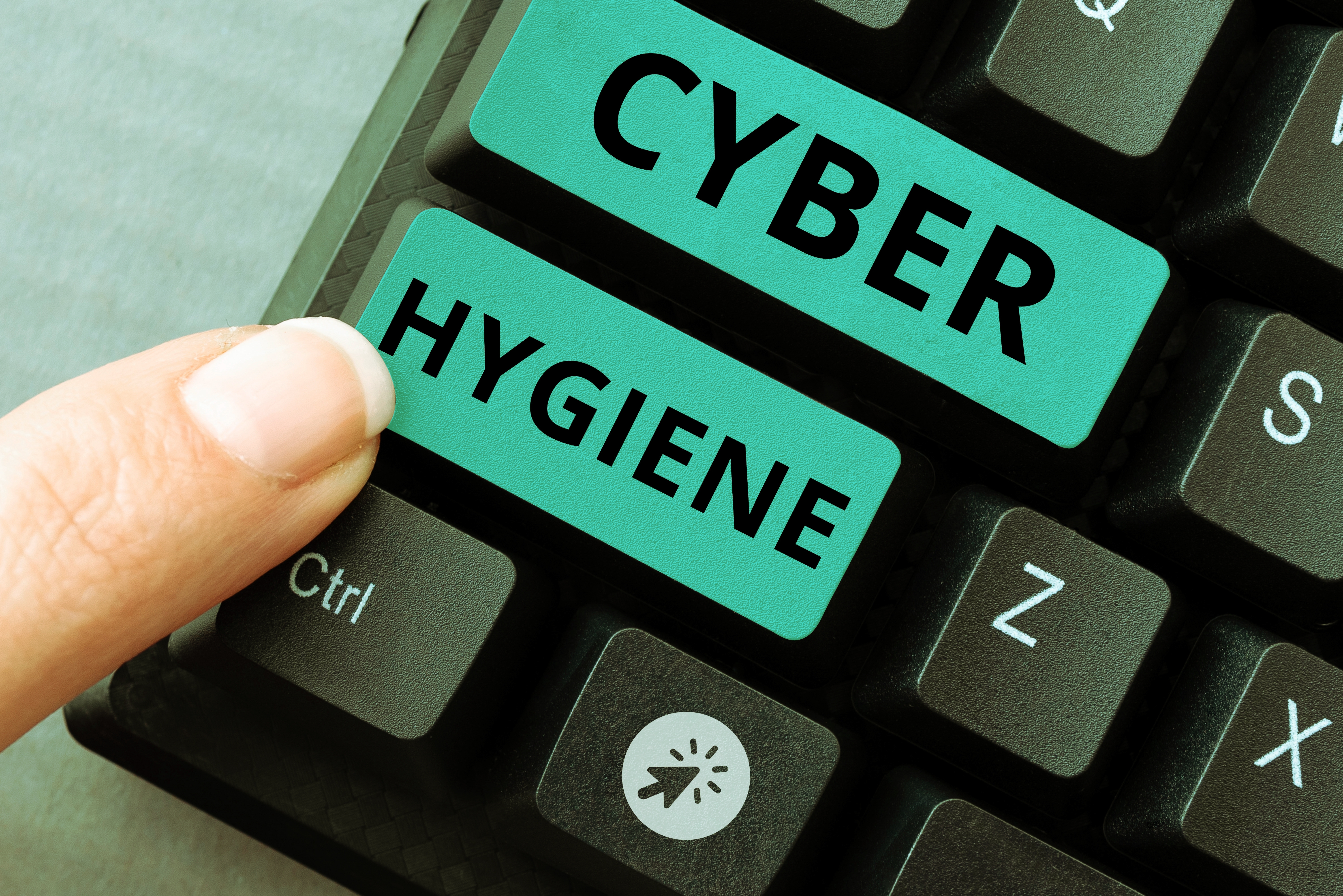 Finger pressing turquoise keys labeled "CYBER" and "HYGIENE" on a keyboard, emphasizing cyber hygiene importance.