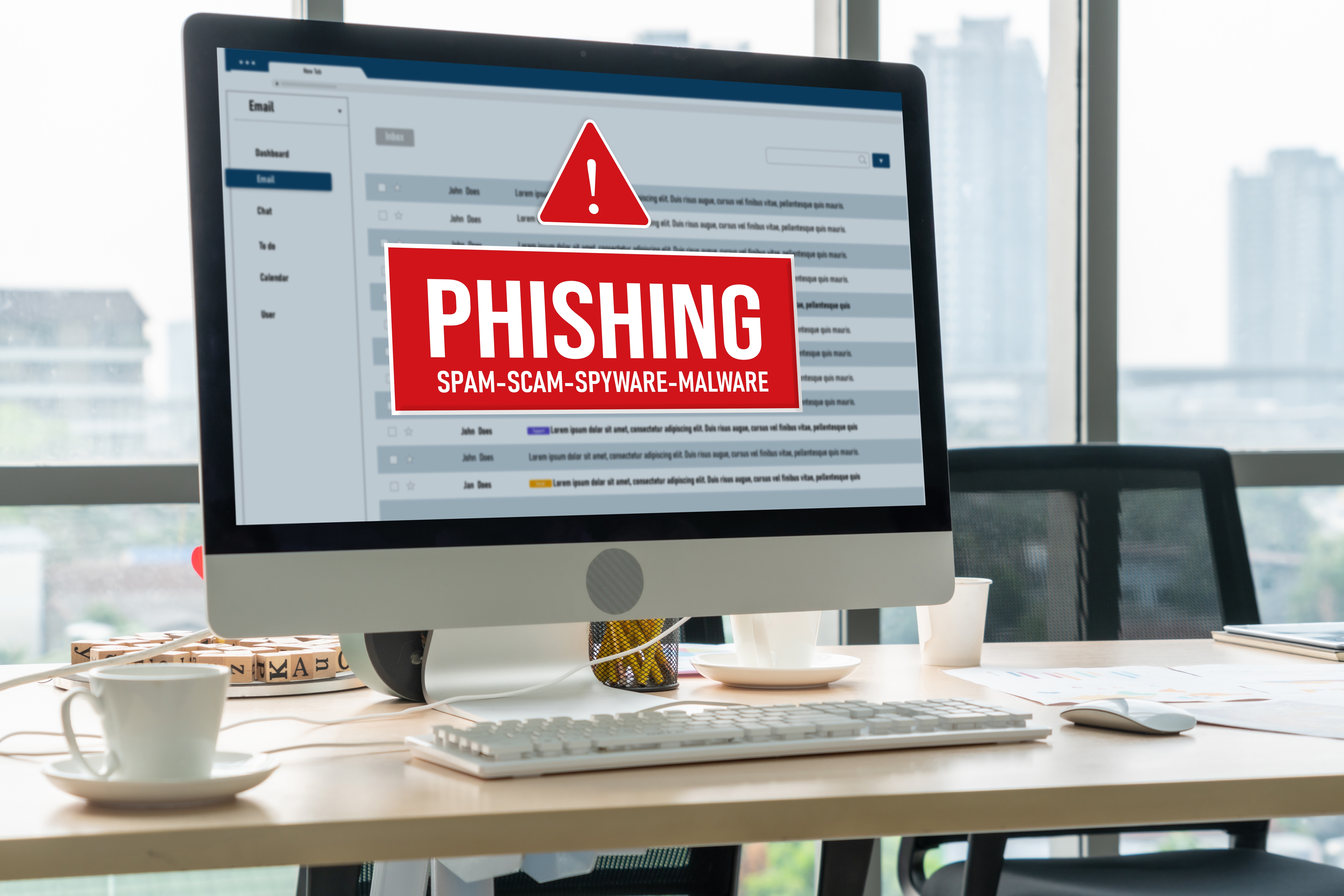 Computer screen showing a "PHISHING" warning over a blurred email inbox. Office setting with cityscape visible through large windows.